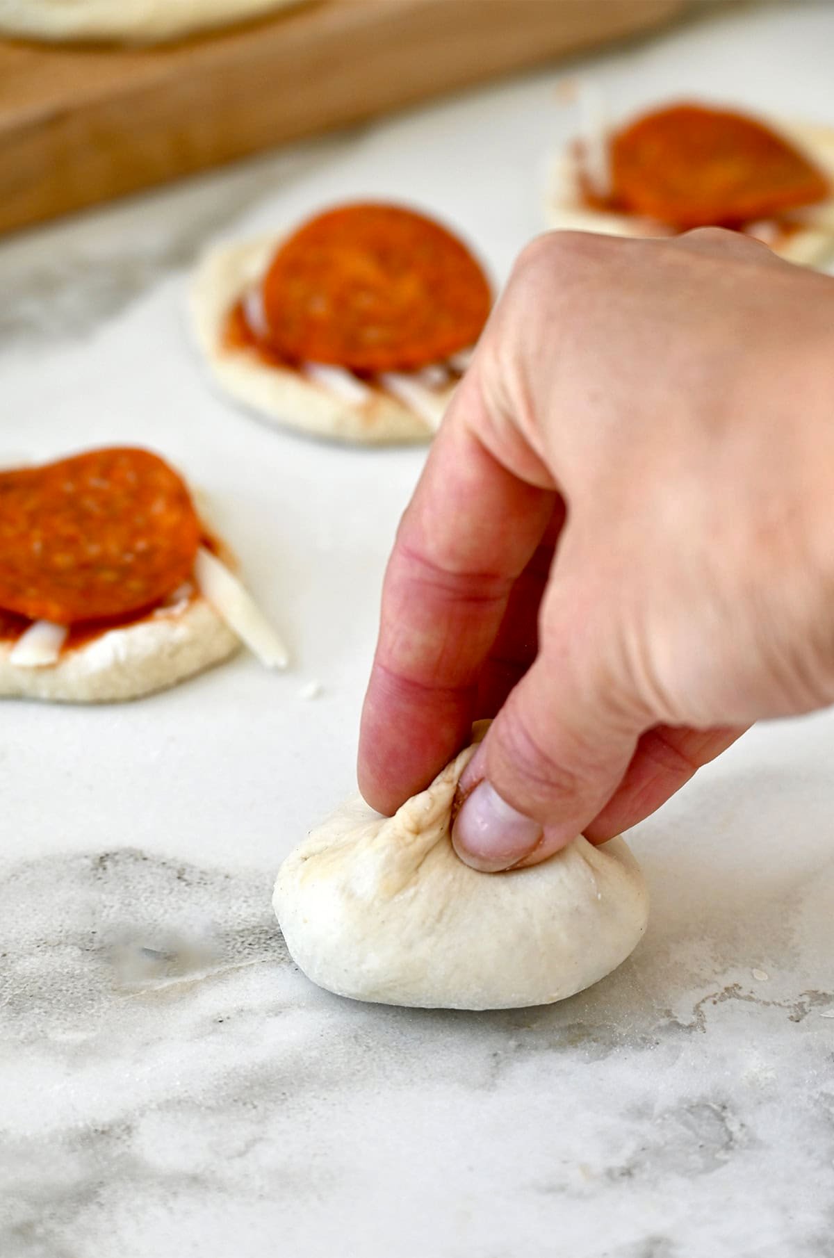 Pinching pizza dough filled with marinara, cheese and pepperoni to form a bite-sized pouch.