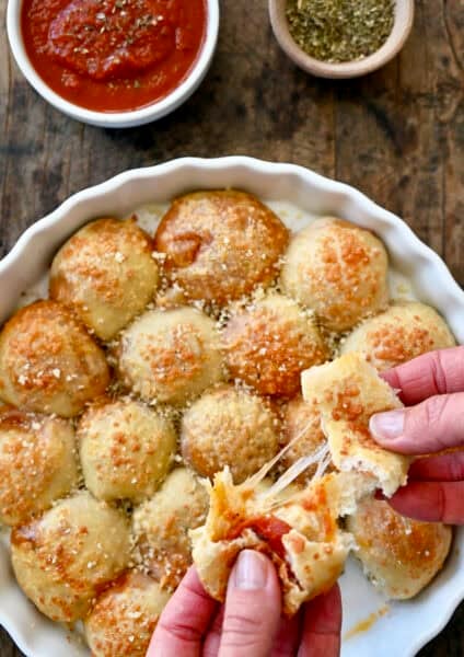 A pizza bite being pulled apart to expose the gooey mozzarella cheese and pepperoni center.