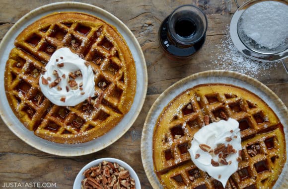 Pumpkin Spice Waffles sprinkled with powdered sugar topped with maple syrup, whipped cream and chopped pecans