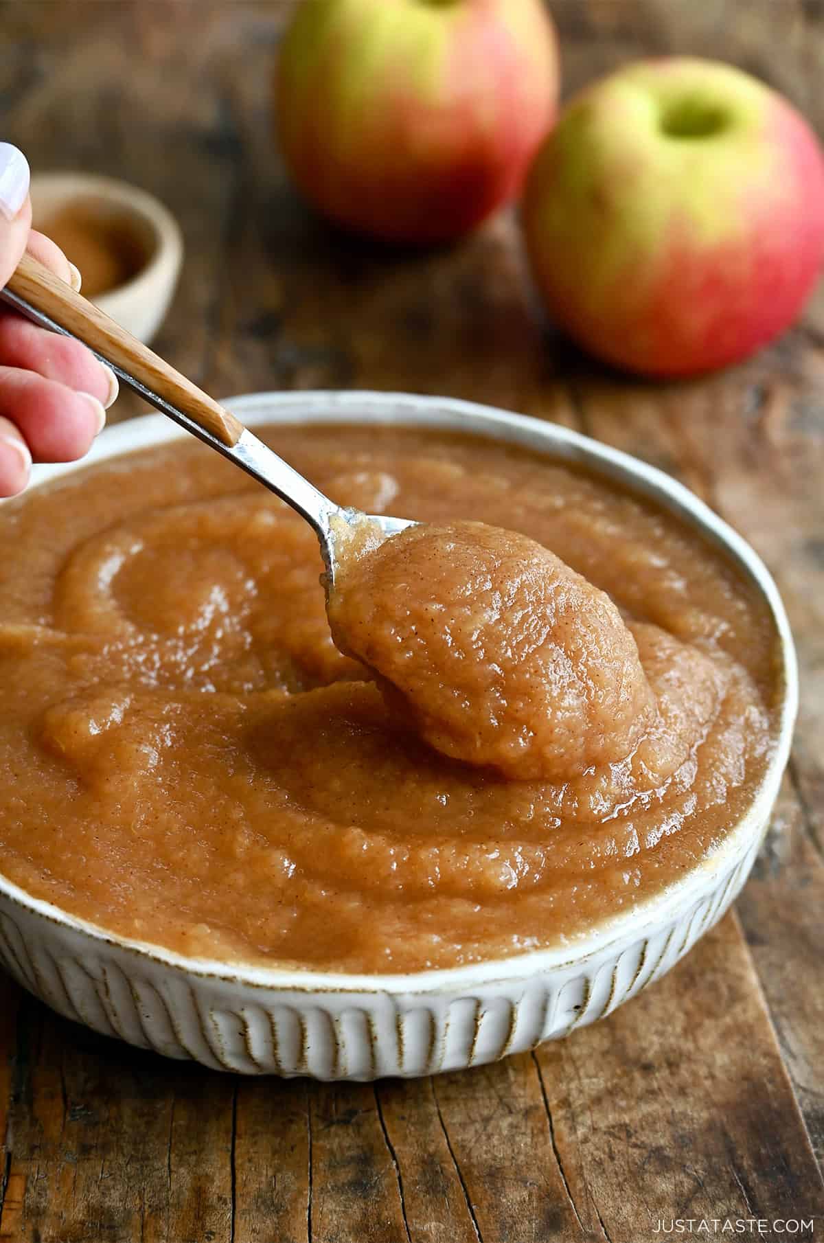 A spoon dips into a bowl containing homemade cinnamon applesauce.
