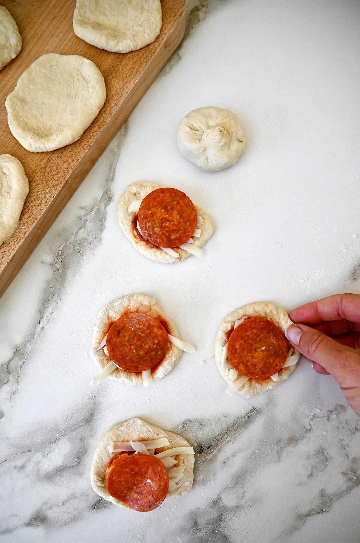 Adding marinara sauce, shredded mozzarella cheese and pepperoni atop mini pizza dough circles.