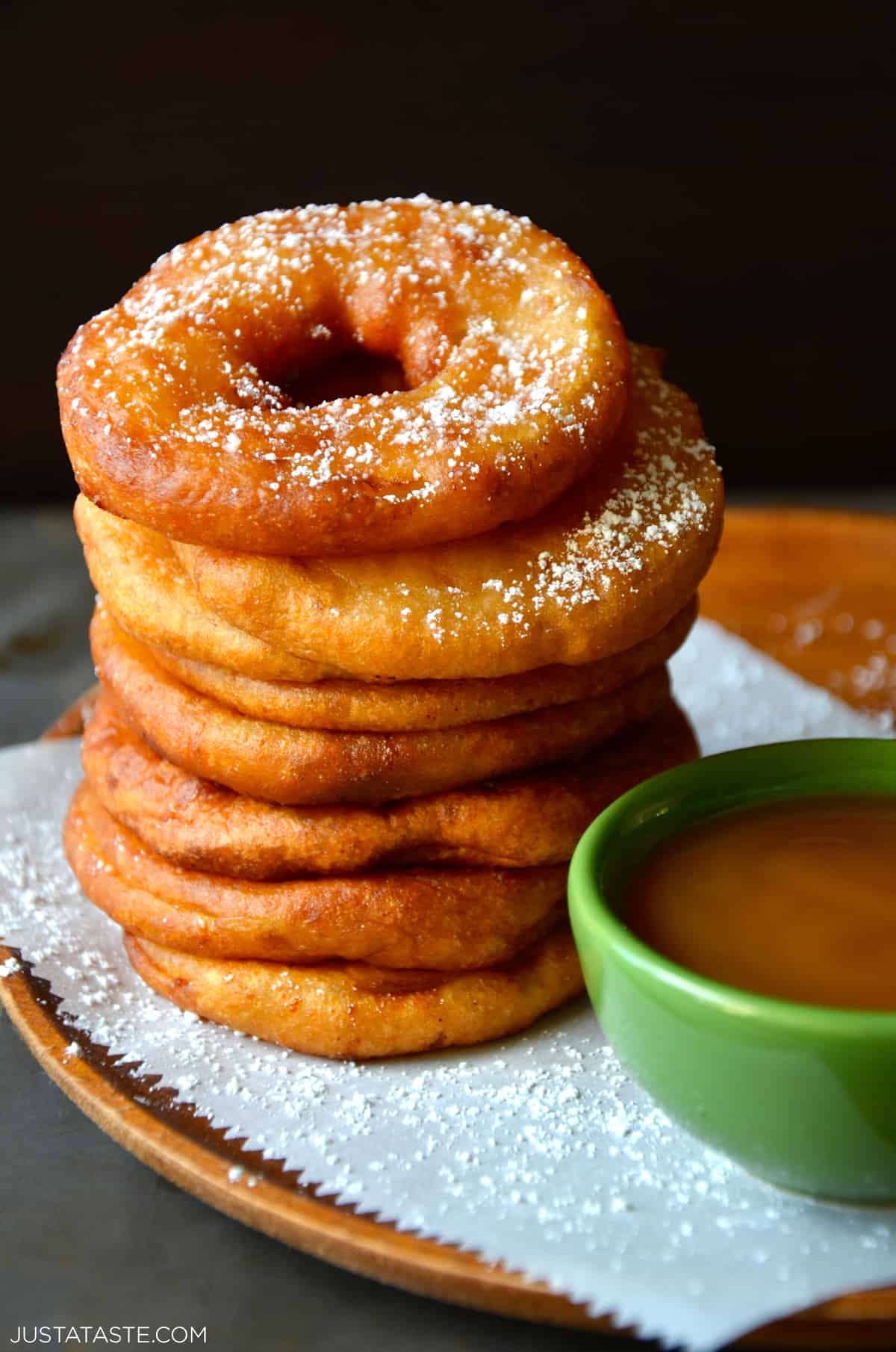 A tall stack of deep fried apple fritter rings next to a small green bowl filled with caramel sauce.