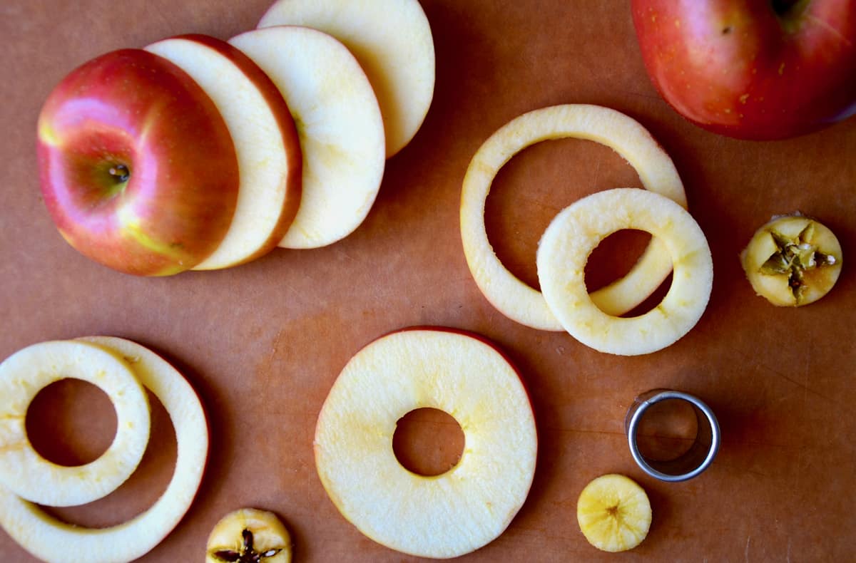 Cored apple rings on a cutting board next to a small circular cookie cutter.
