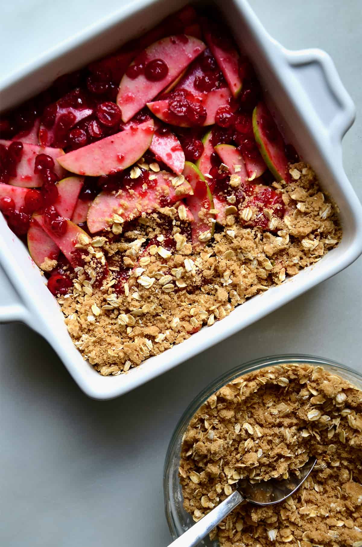 A square baking dish containing apple slices and cranberry sauce topped with oat crisp topping.