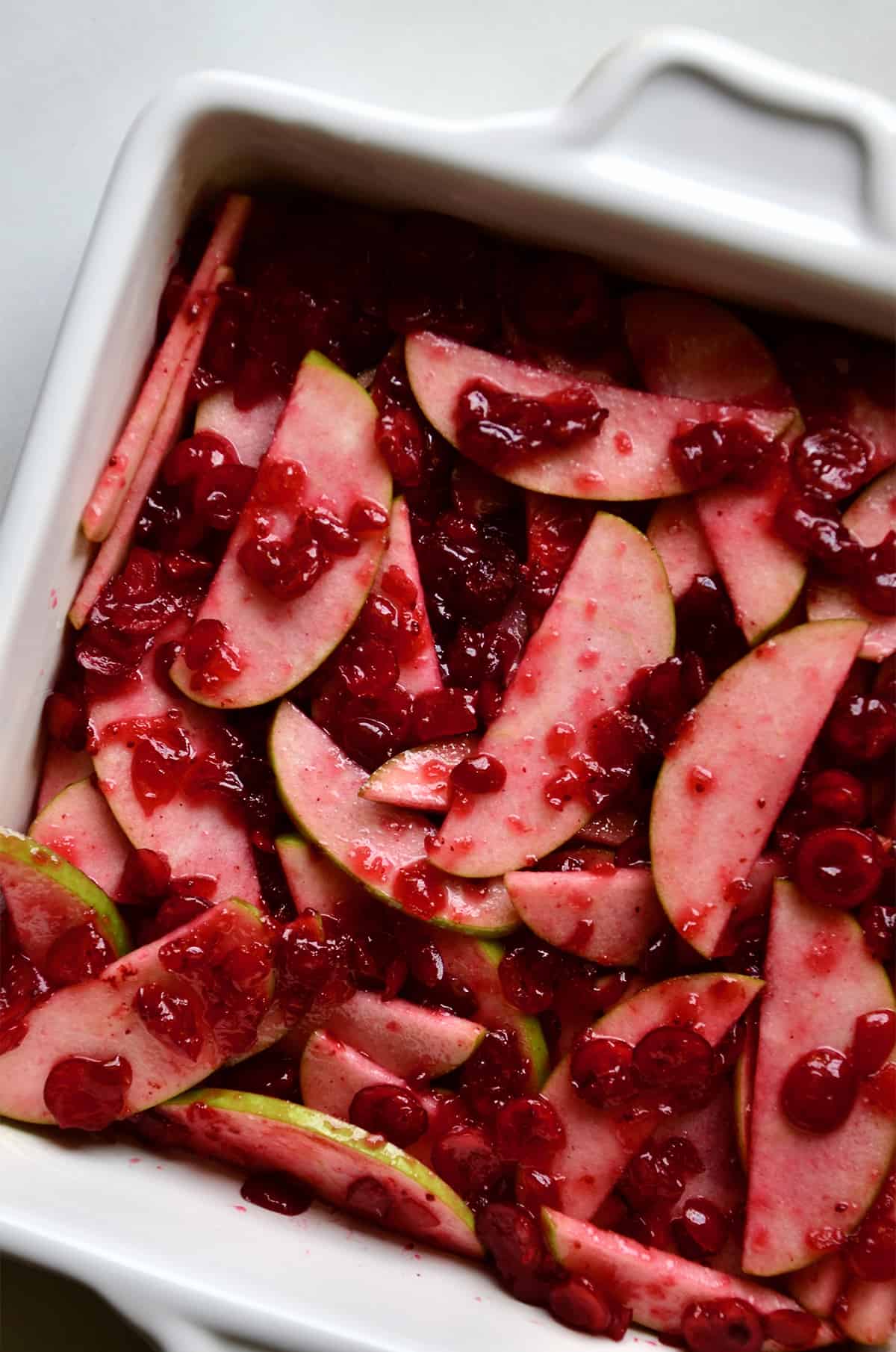 A baking dish containing apple slices and cranberry sauce.