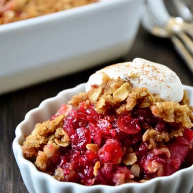 Cranberry apple crisp topped with whipped cream in an oval ramekin.