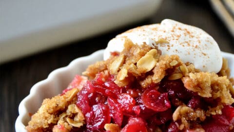 Cranberry apple crisp topped with whipped cream in an oval ramekin.