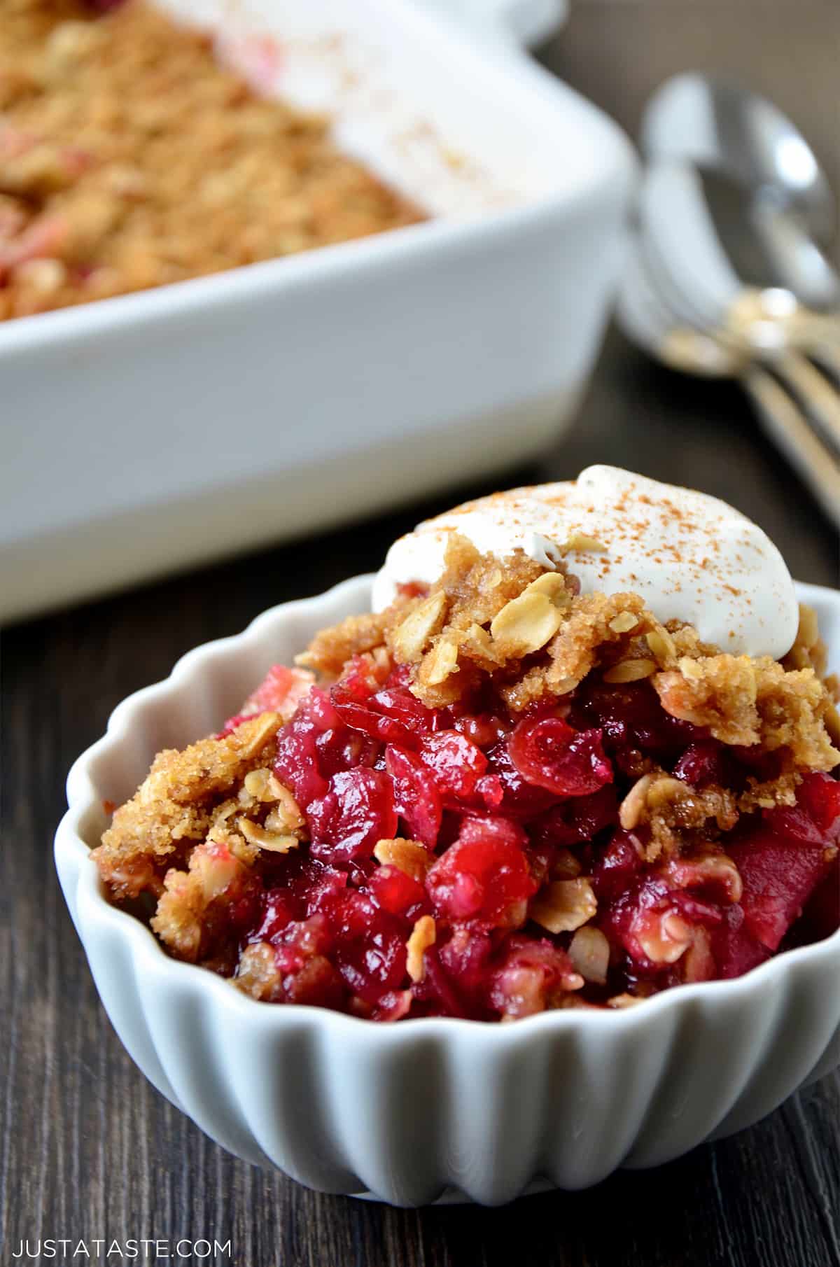 Cranberry apple crisp topped with whipped cream in an oval ramekin. 