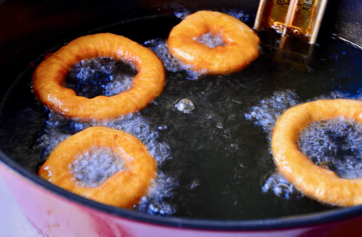Apple fritters being fried in oil in a large stockpot.