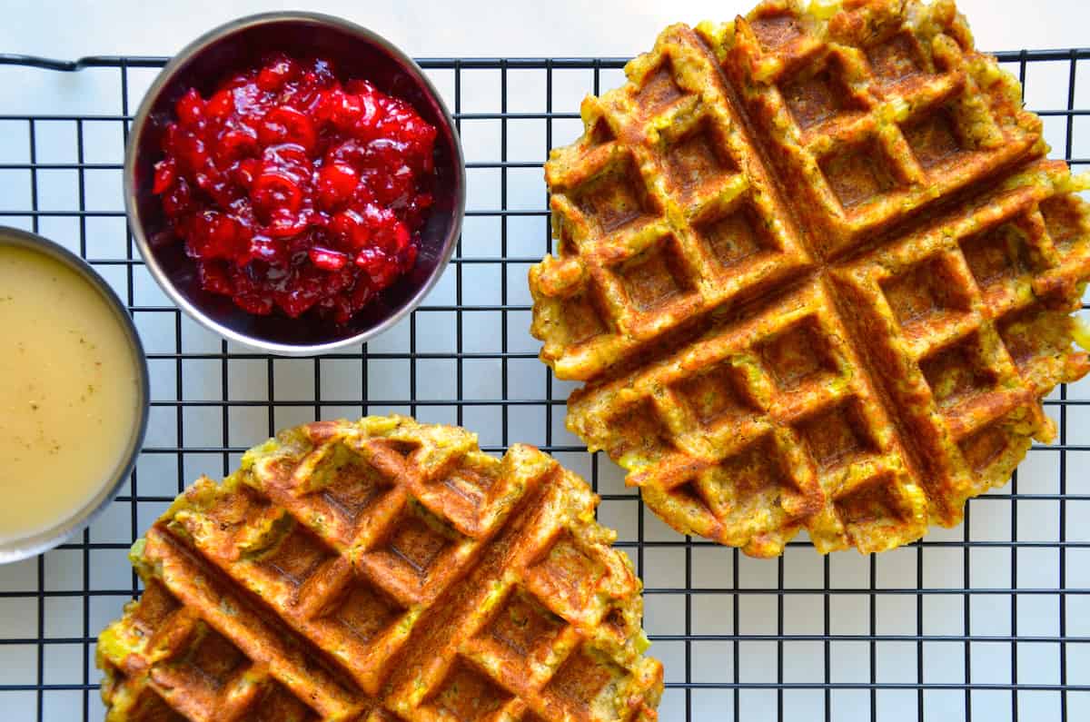Two stuffing waffles on a wire cooling rack next to a small bowl containing cranberry sauce.