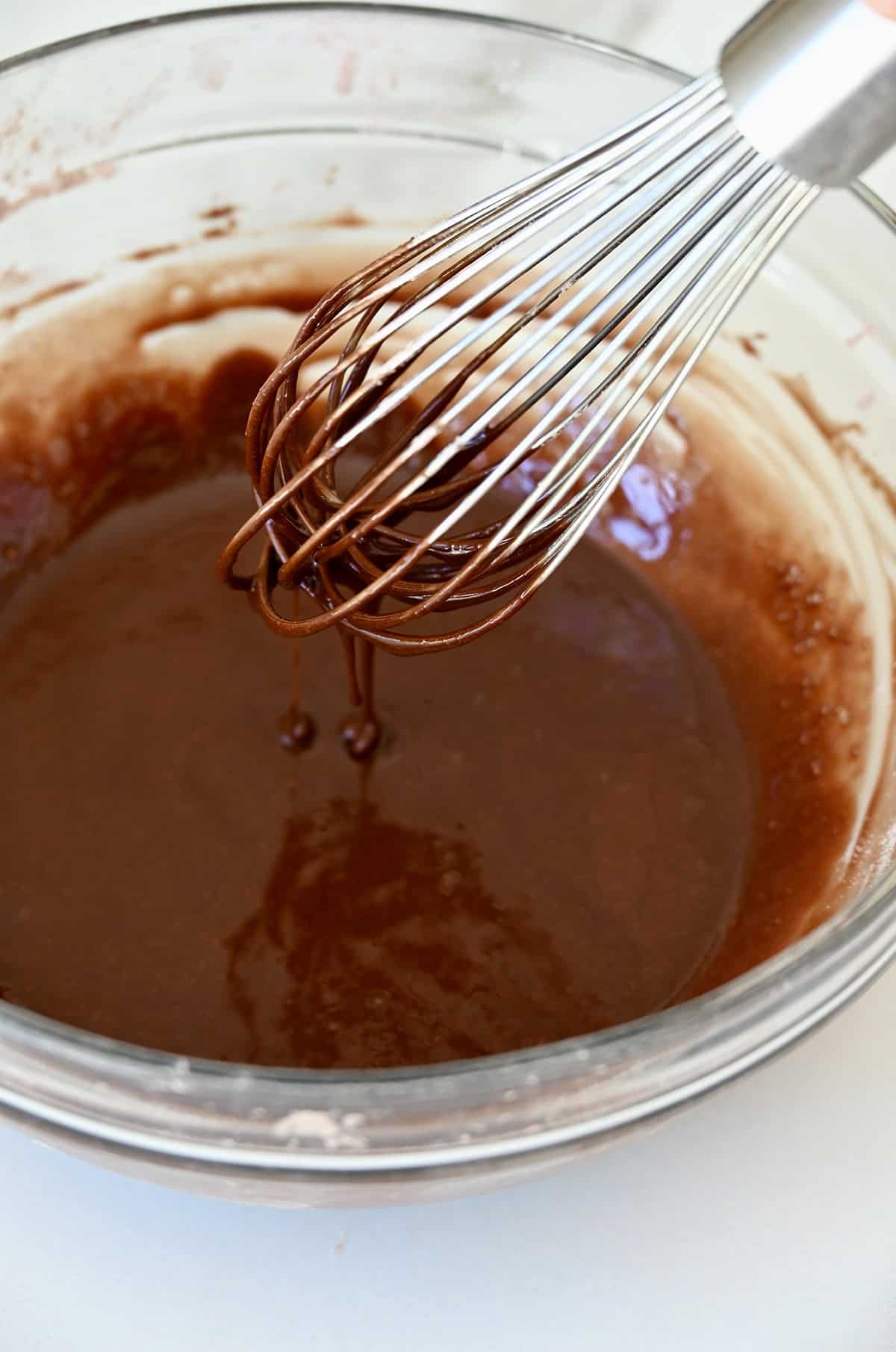 Silky smooth chocolate glaze in a bowl with a whisk.