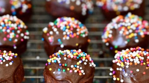 Glazed chocolate doughnut holes with rainbow sprinkles on a wire cooling rack.