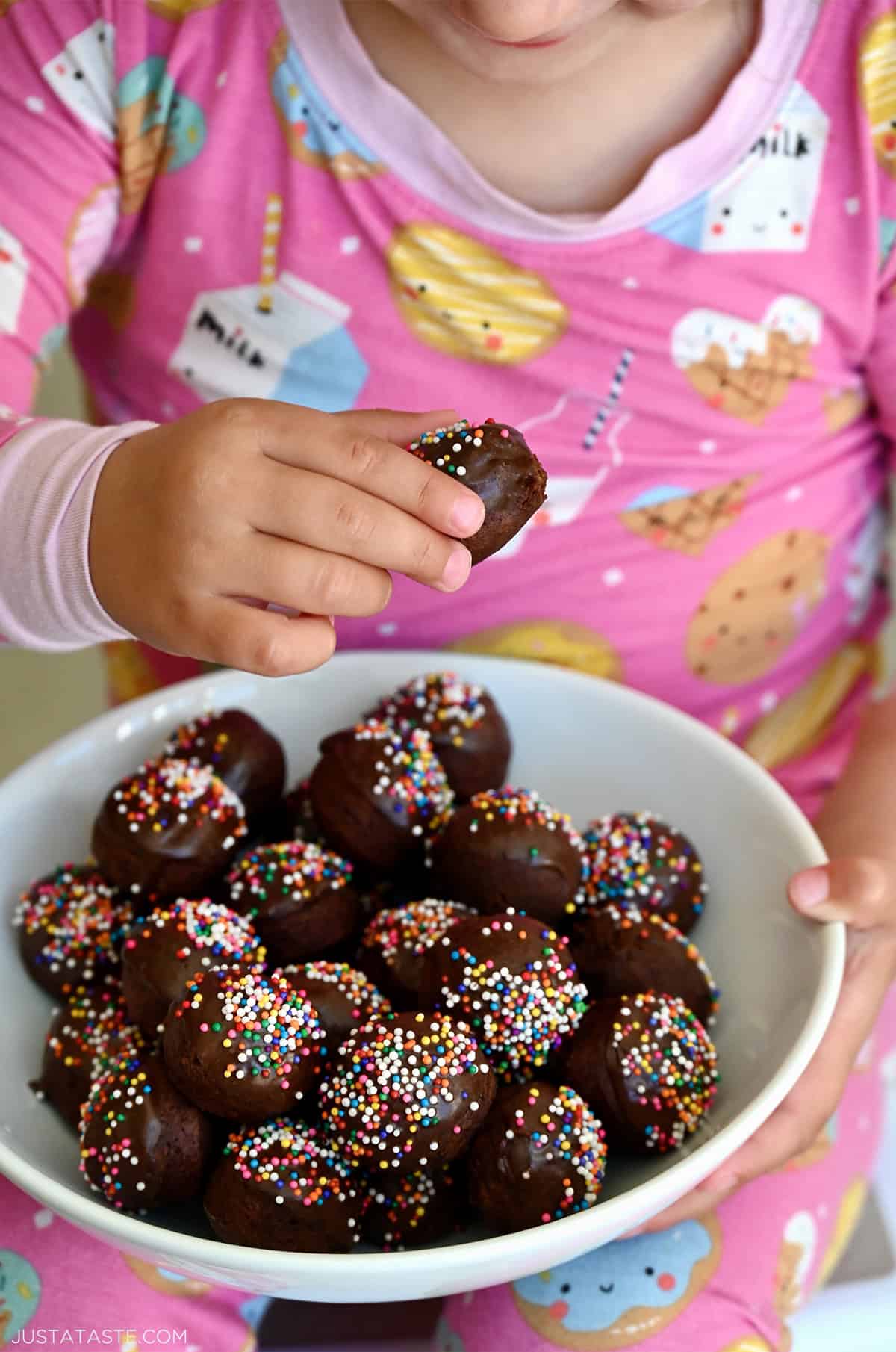 Glazed chocolate doughnut holes in a bowl that a child is holding.