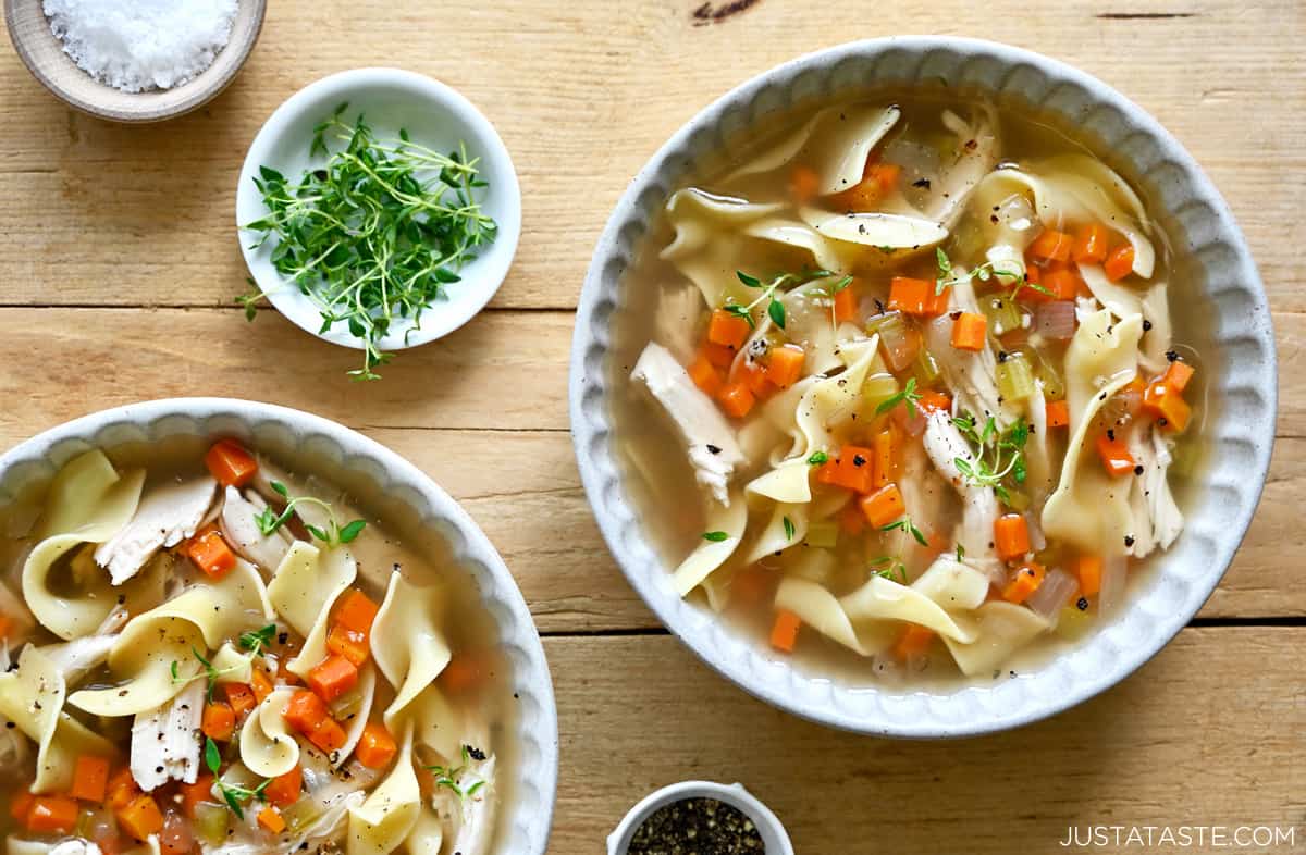 Two bowls containing homemade chicken noodle soup garnished with micro greens.