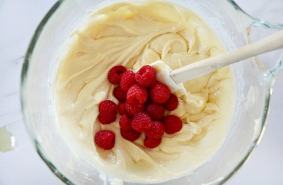 Glass bowl containing coffee cake batter, fresh raspberries and spatula