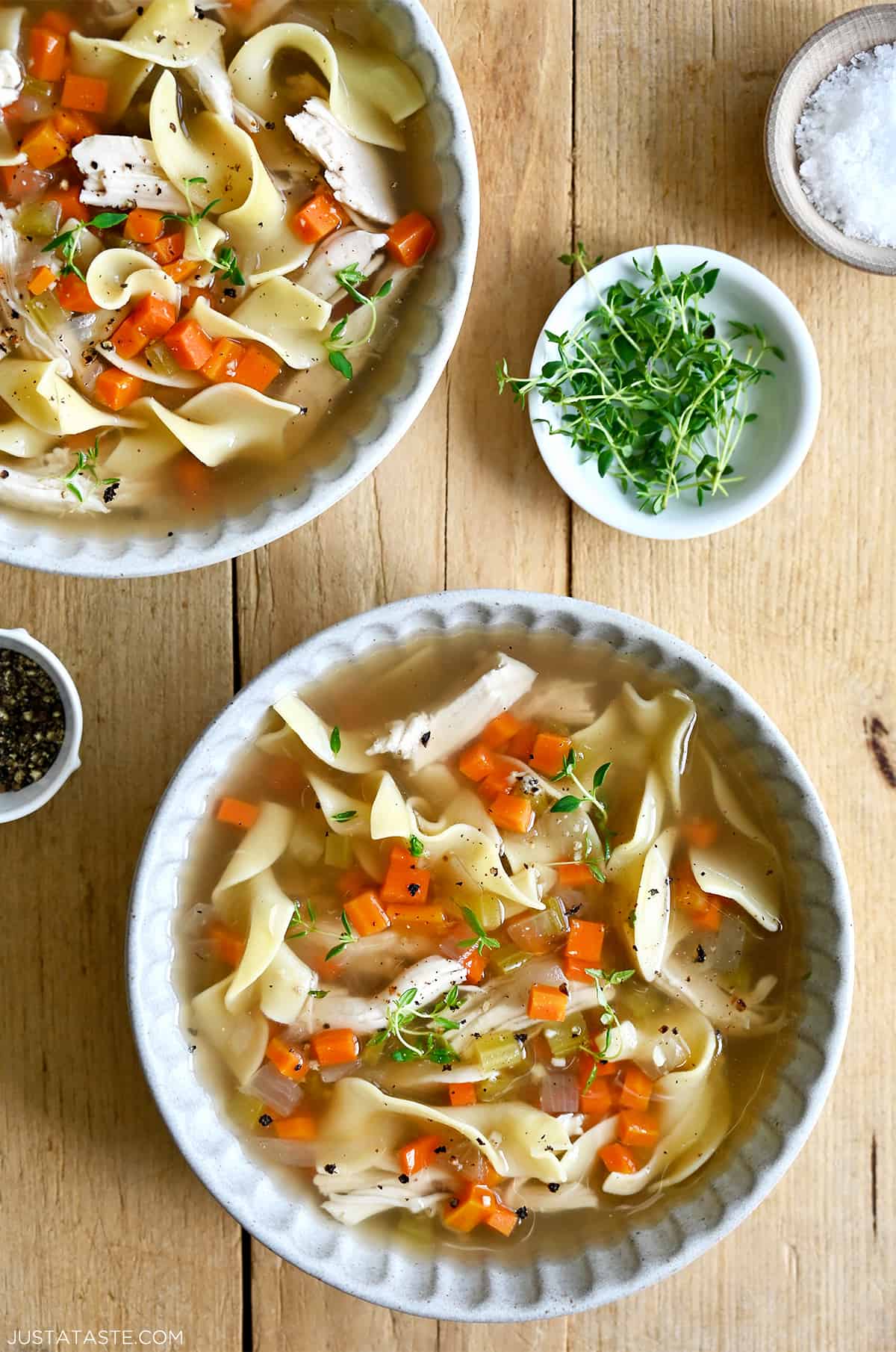 Two bowls containing chicken noodle soup next to a small bowl containing micro greens.