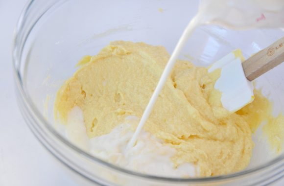 A clear bowl with pancake batter and milk being poured in