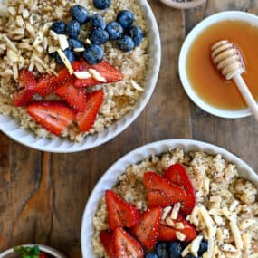 Two bowls containing creamy quinoa topped with fresh strawberries, blueberries, slivered almonds and chia seeds.