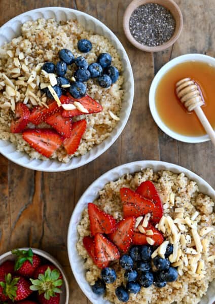 Two bowls containing creamy quinoa topped with fresh strawberries, blueberries, slivered almonds and chia seeds.