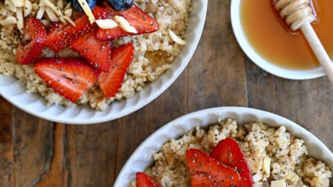 Two bowls containing creamy quinoa topped with fresh strawberries, blueberries, slivered almonds and chia seeds.