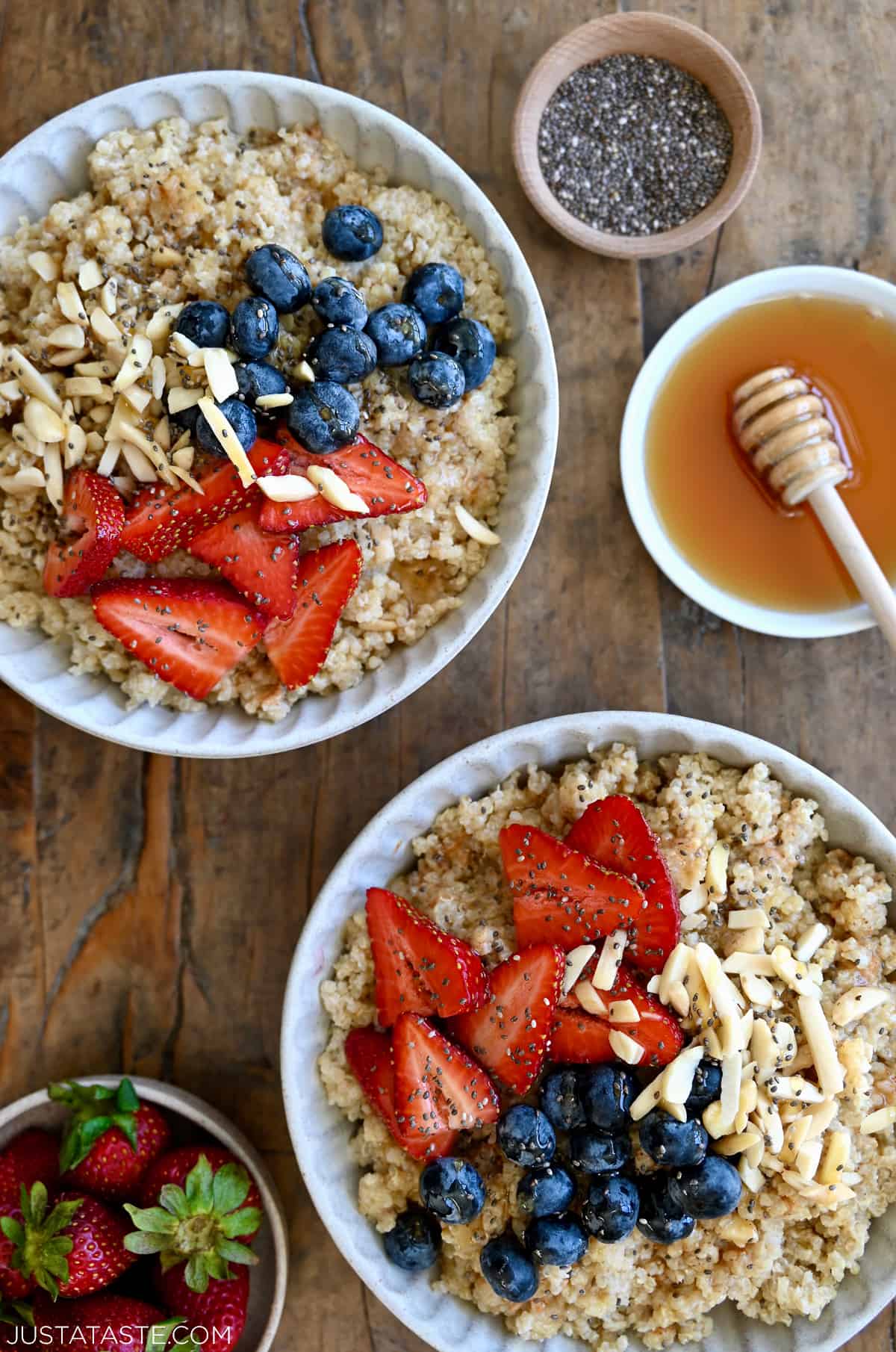 Two bowls containing creamy quinoa topped with fresh strawberries, blueberries, slivered almonds and chia seeds.