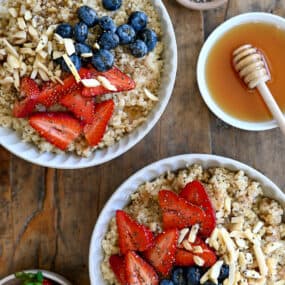 A top-down view of two Quinoa Breakfast Bowls topped with fresh strawberries and blueberries, chopped nuts and chia seeds