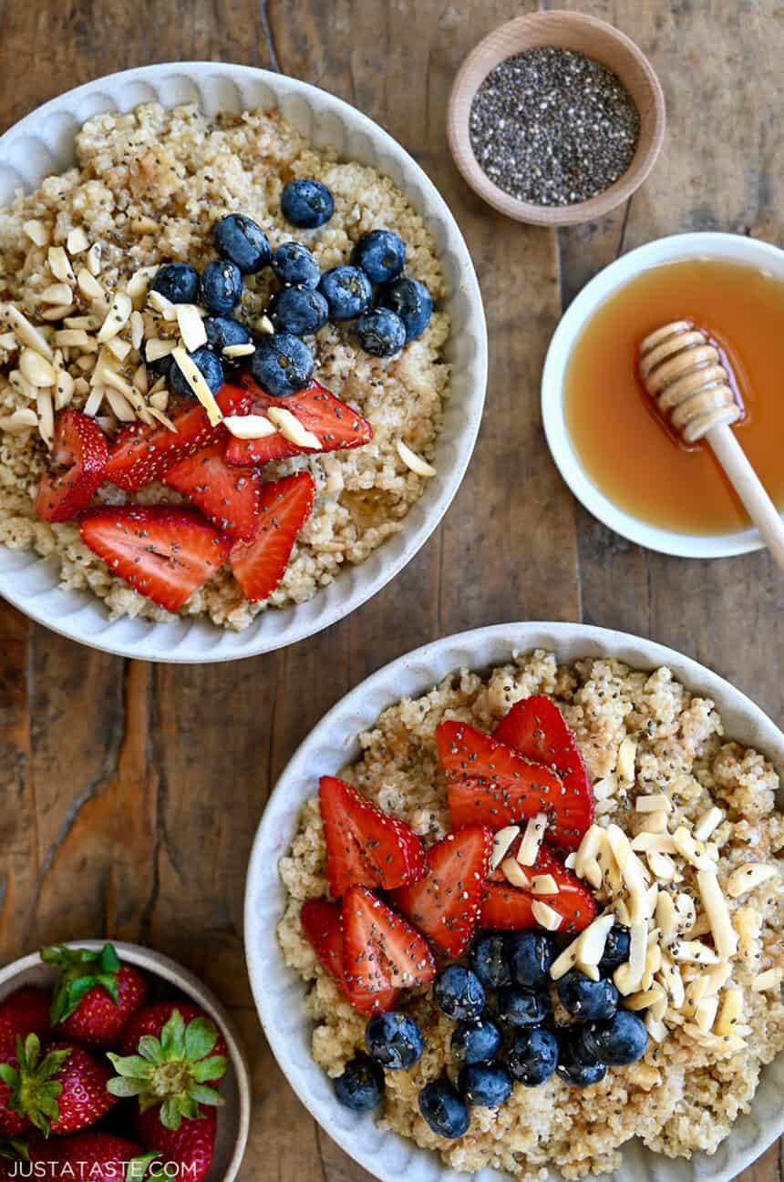 A top-down view of two Quinoa Breakfast Bowls topped with fresh strawberries and blueberries, chopped nuts and chia seeds