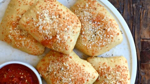 Homemade pizza pockets on a plate with a small bowl containing marinara sauce.