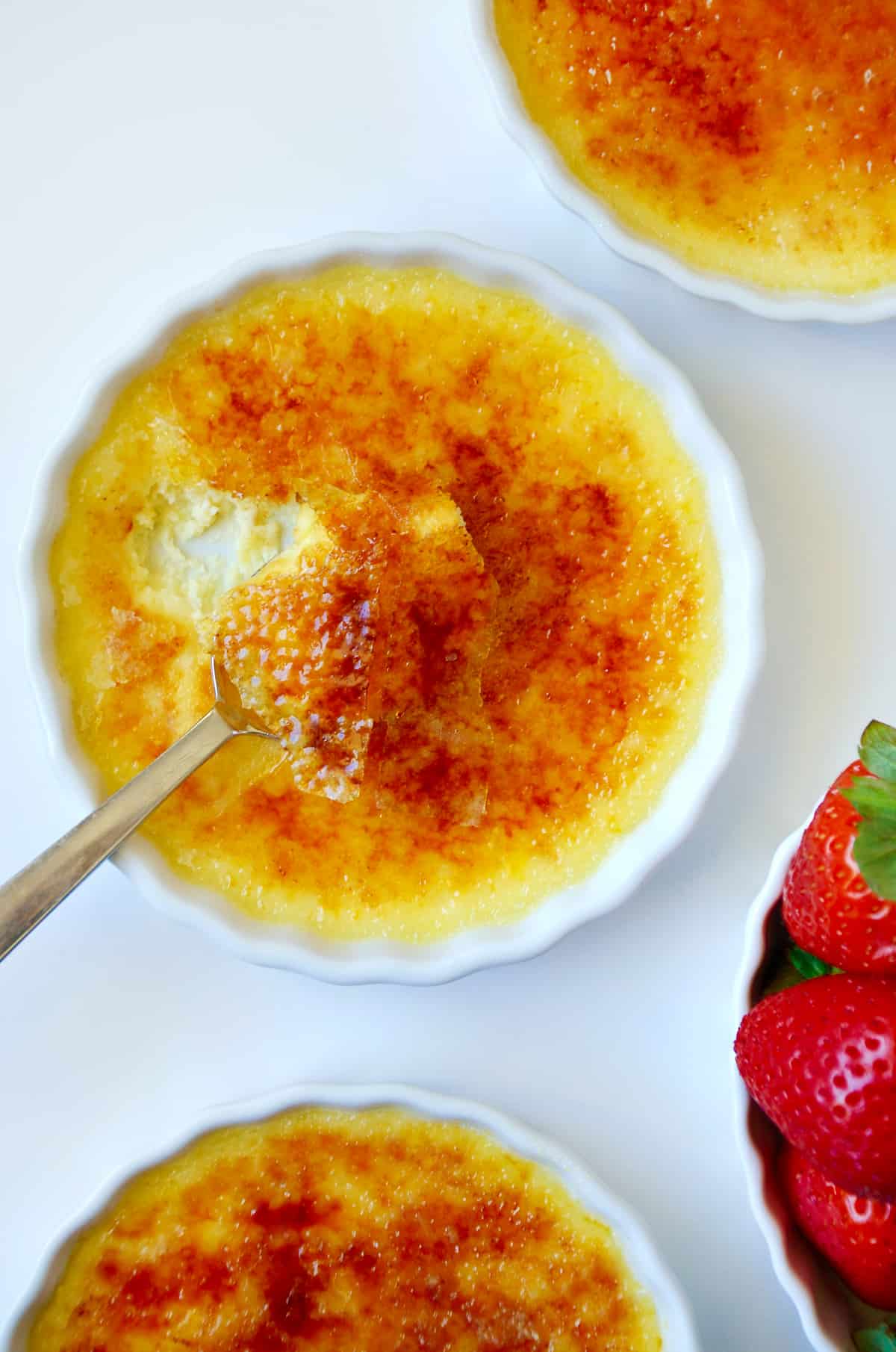 A crème brûlée cheesecake in a white tart dish next to a bowl of strawberries.