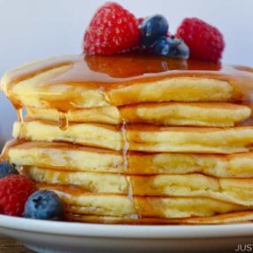 A stack of ricotta pancakes with fruit and syrup on top