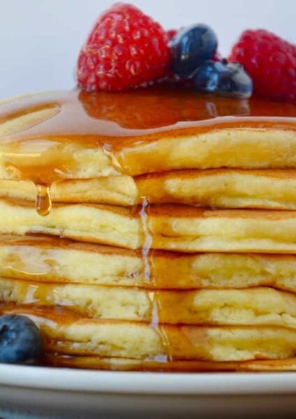 A stack of ricotta pancakes with fruit and syrup on top
