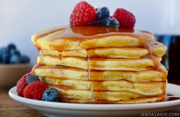 A stack of ricotta pancakes with fruit and syrup on top