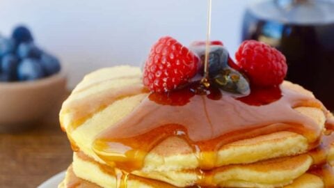 A white plate containing a stack of ricotta pancakes topped with syrup