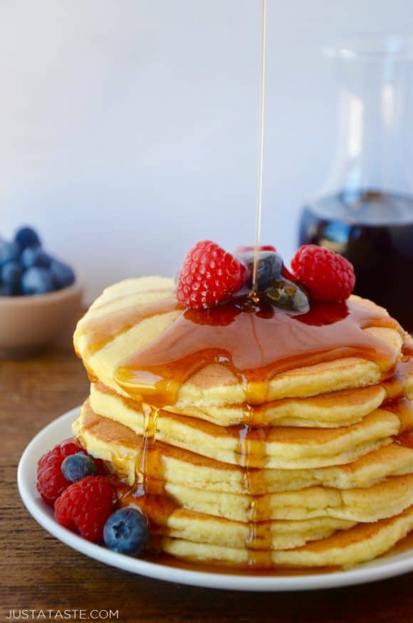 A white plate containing a stack of ricotta pancakes topped with syrup