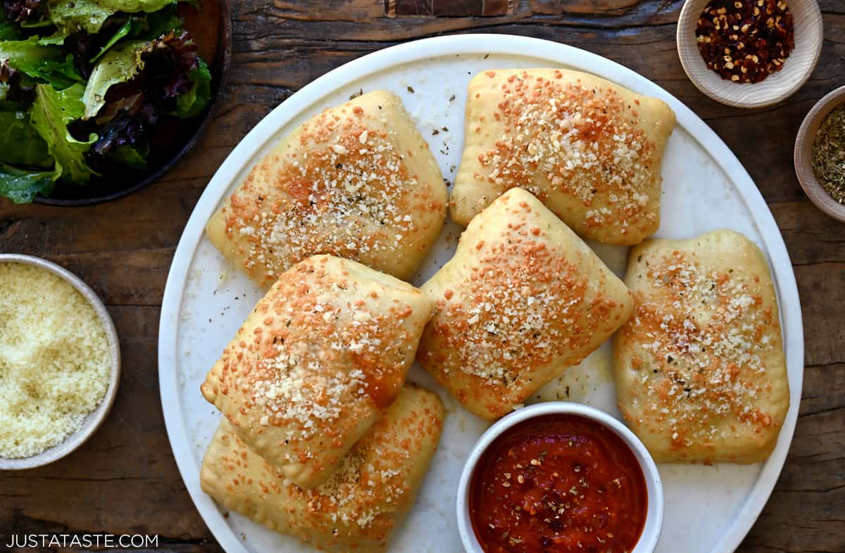 Several homemade hot pockets on a white dinner plate next to a small bowl containing marinara sauce.