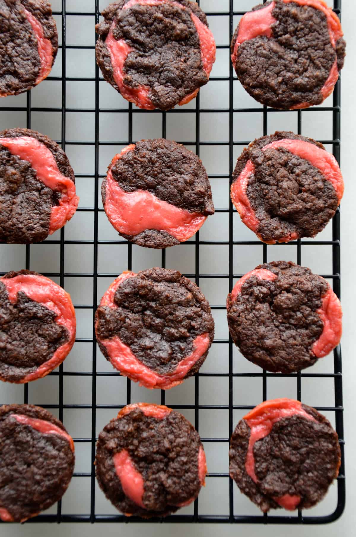 Three rows of raspberry cheesecake-swirled brownie bites cooling on a wire baking rack.