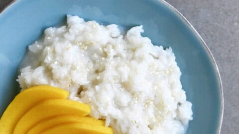 Coconut sticky rice with slices of fresh mango on a light blue plate.