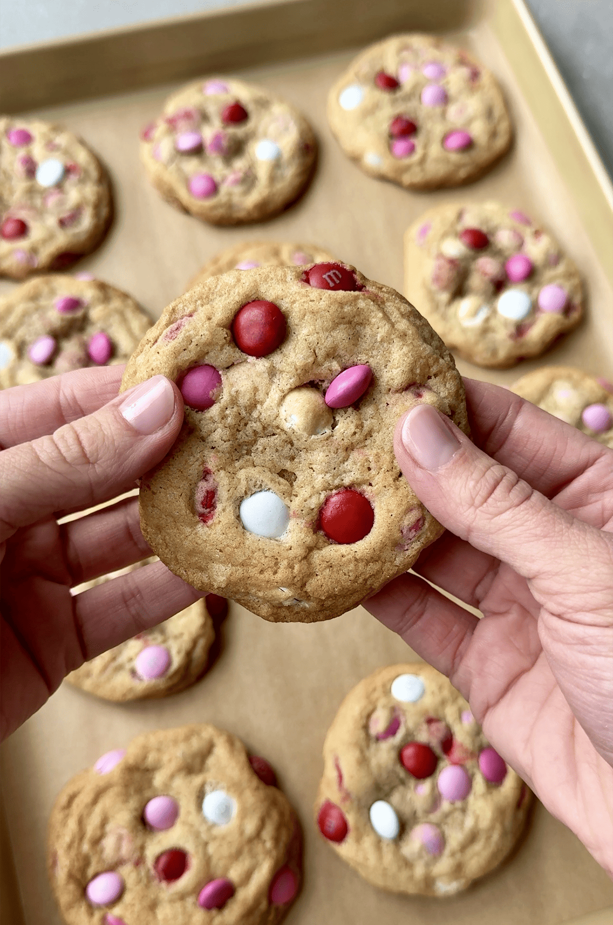 A hand holds a cookie studded with red, pink and white M&M candies.