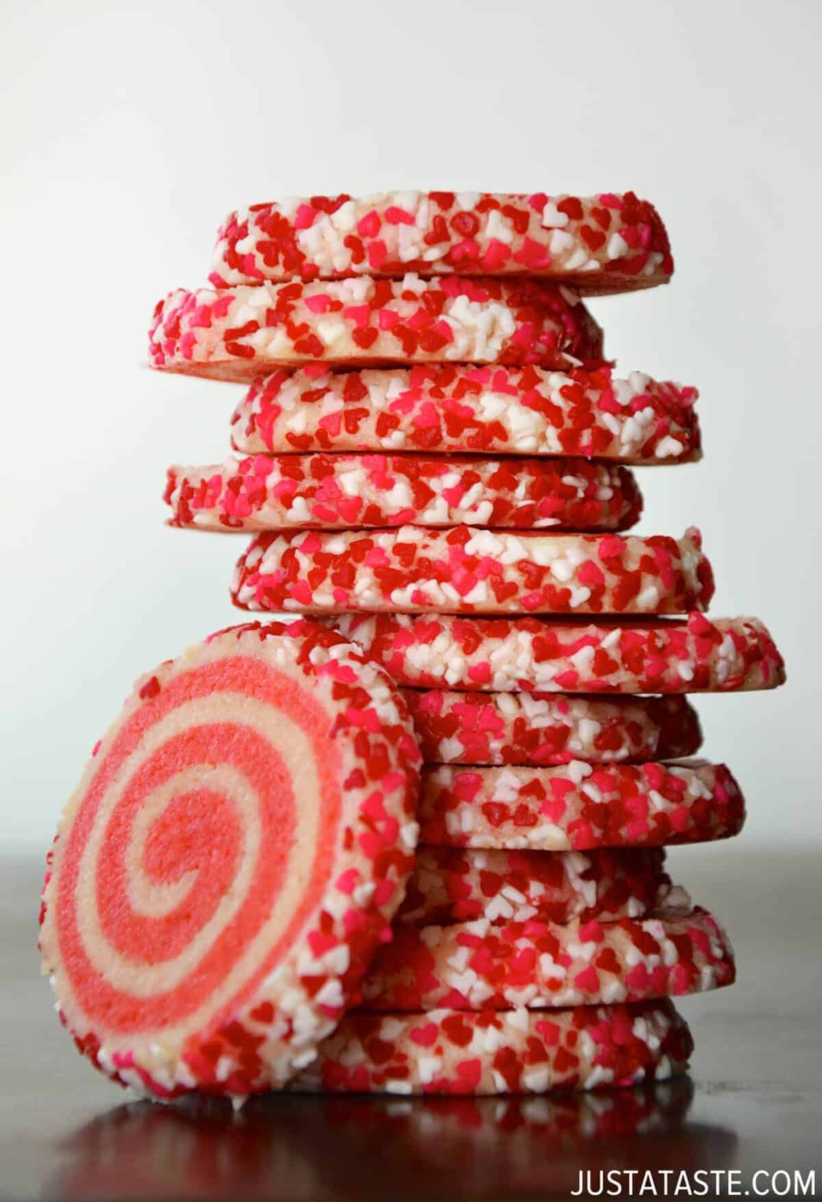 A tall stack of pink pinwheel sugar cookies with heart-shaped sprinkles.