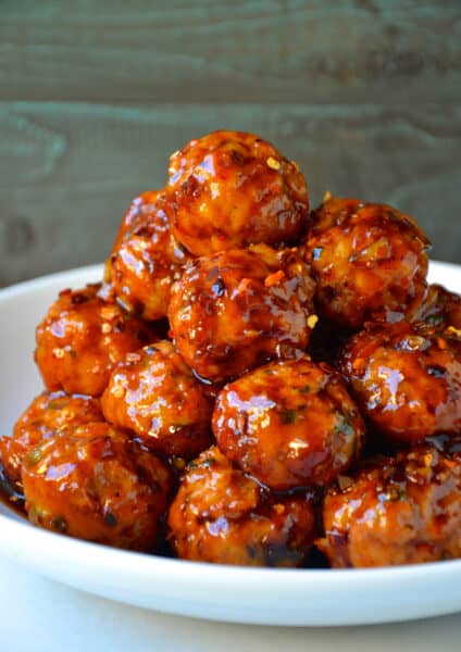 A tall stack of orange chicken meatballs with crushed red pepper flakes in a white bowl.