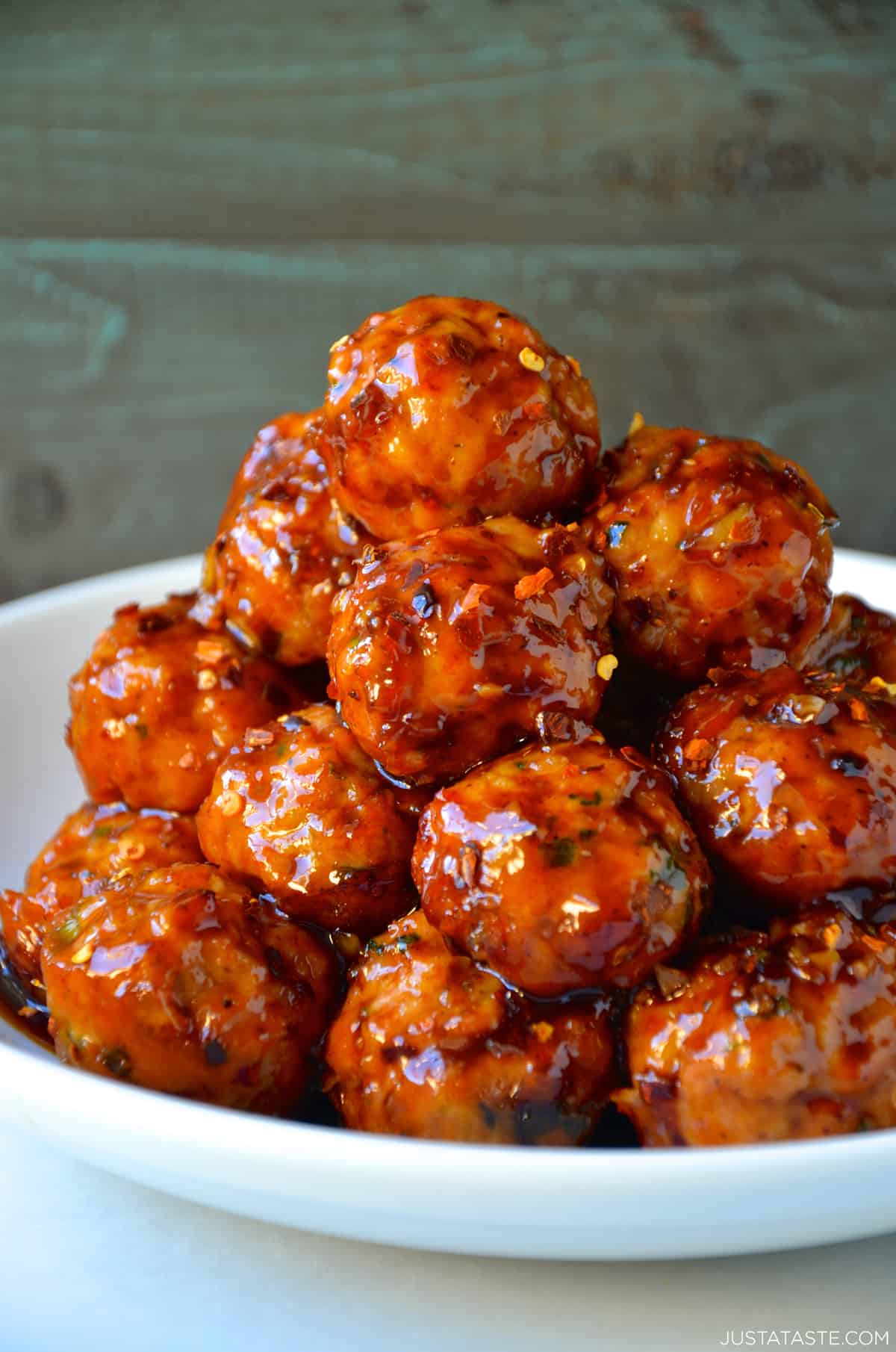 A tall stack of orange chicken meatballs with crushed red pepper flakes in a white bowl.