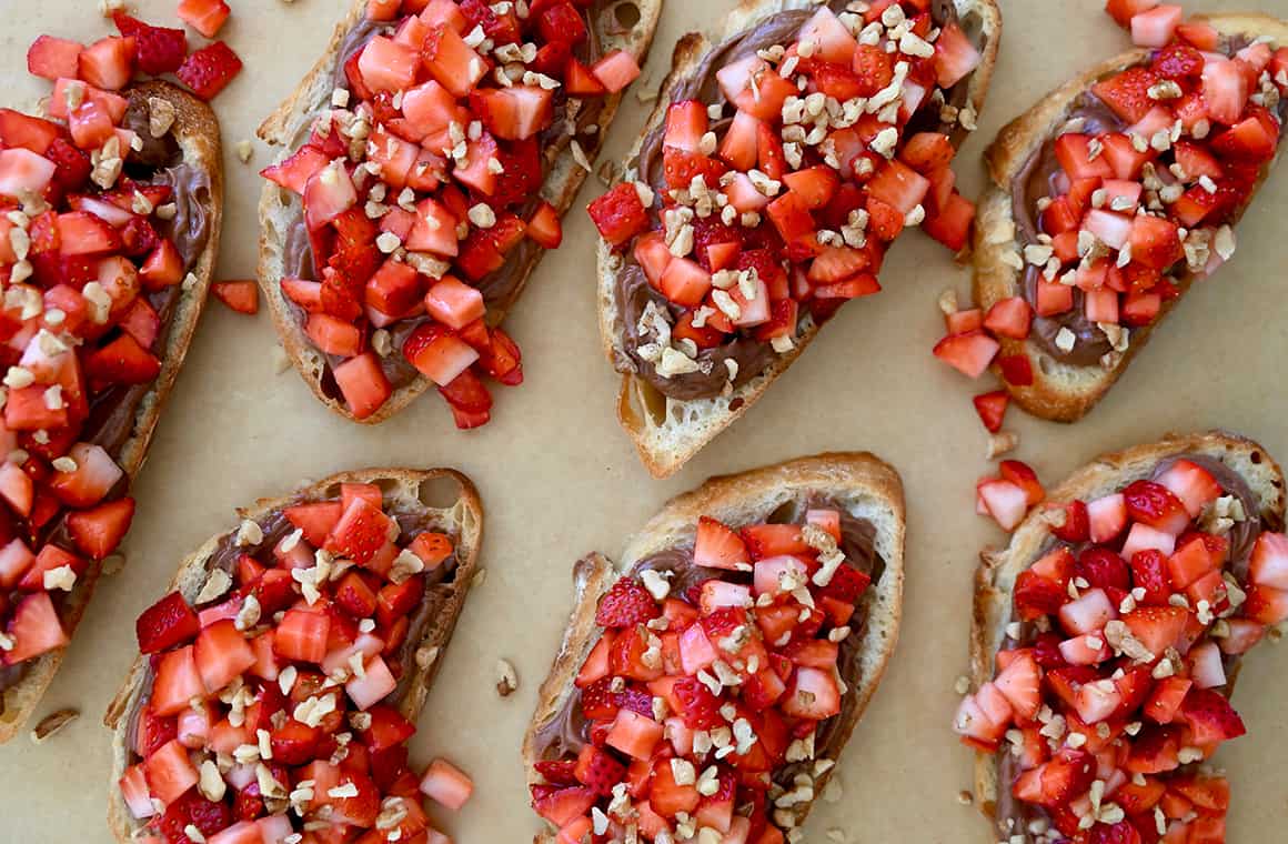 A top-down view of Nutella toasts garnished with fresh diced fruit and chopped walnuts