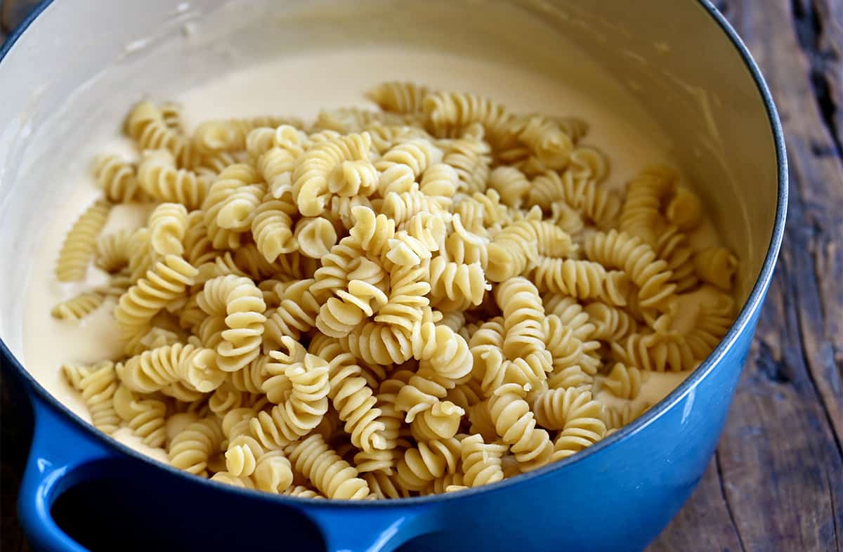 Pasta being added to a large stockpot that contains cheese sauce.