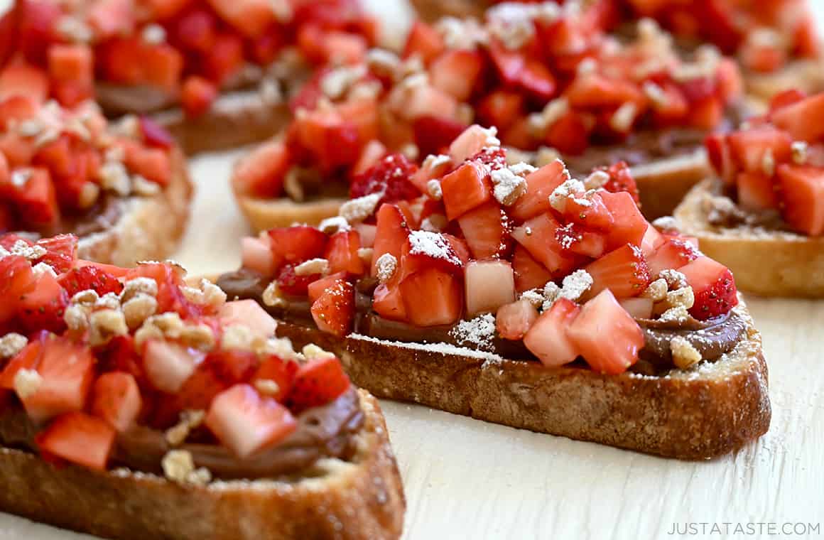 A close-up view of dessert bruschetta featuring toasted baguettes slathered with Nutella and topped with diced fresh strawberries