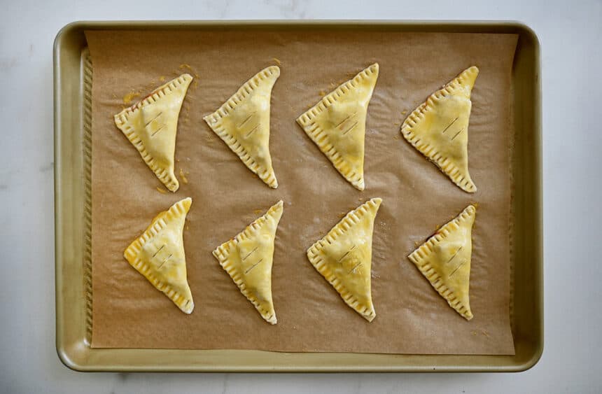Unbaked puff pastry triangles on a parchment paper-lined baking sheet
