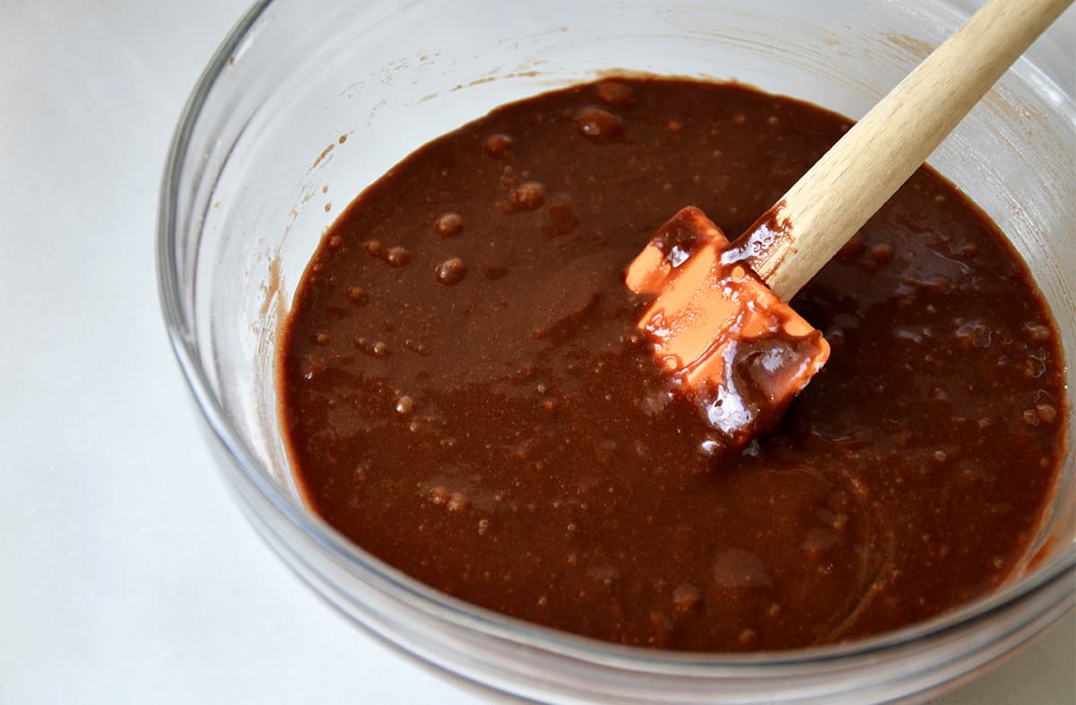 Brownie batter in a glass bowl with an orange spatula.