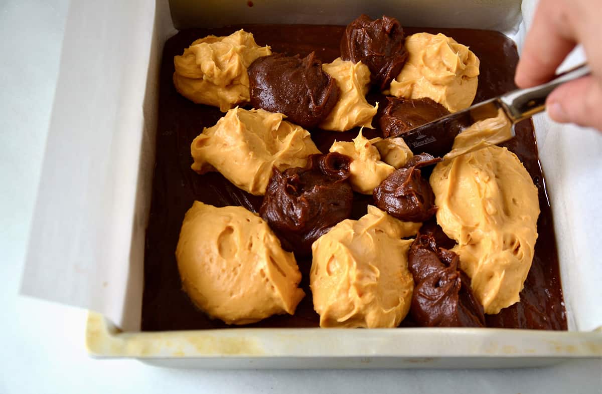 Dollops of butterscotch cheesecake and brownie batter in a parchment paper-lined square baking dish.