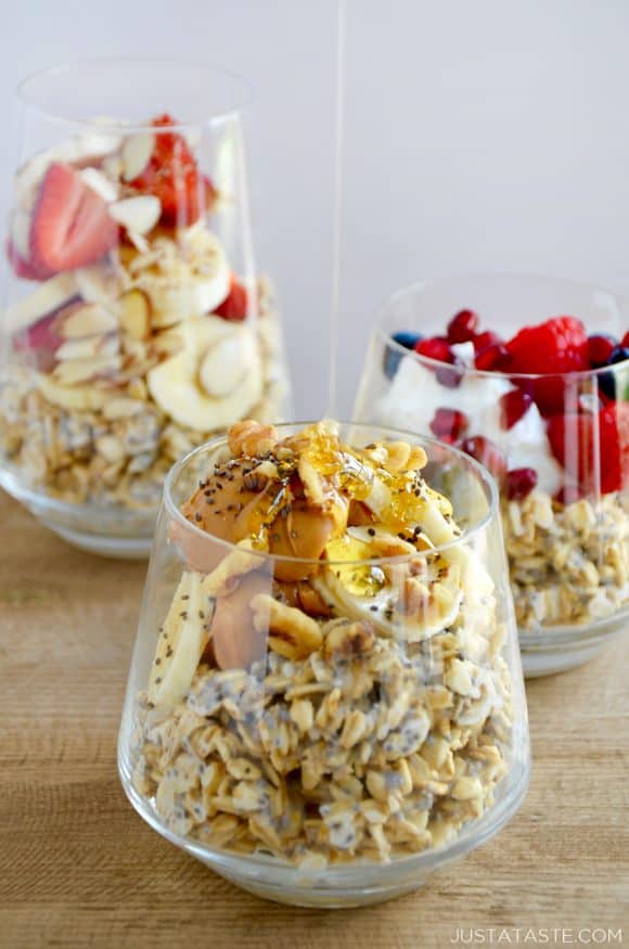 A clear glass containing oats topped with bananas, peanut butter and chia seeds with honey being drizzled on top