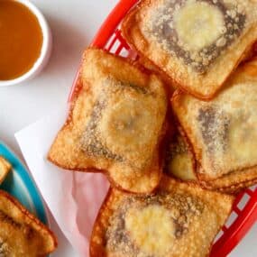 Banana Chocolate Wonton Poppers in a red food basket next to a small bowl filled with caramel sauce