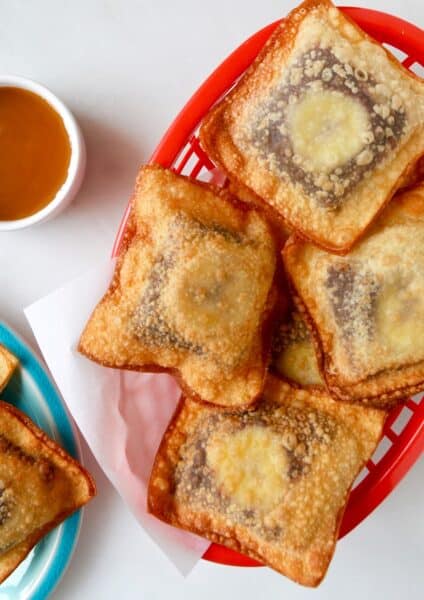 Banana Chocolate Wonton Poppers in a red food basket next to a small bowl filled with caramel sauce